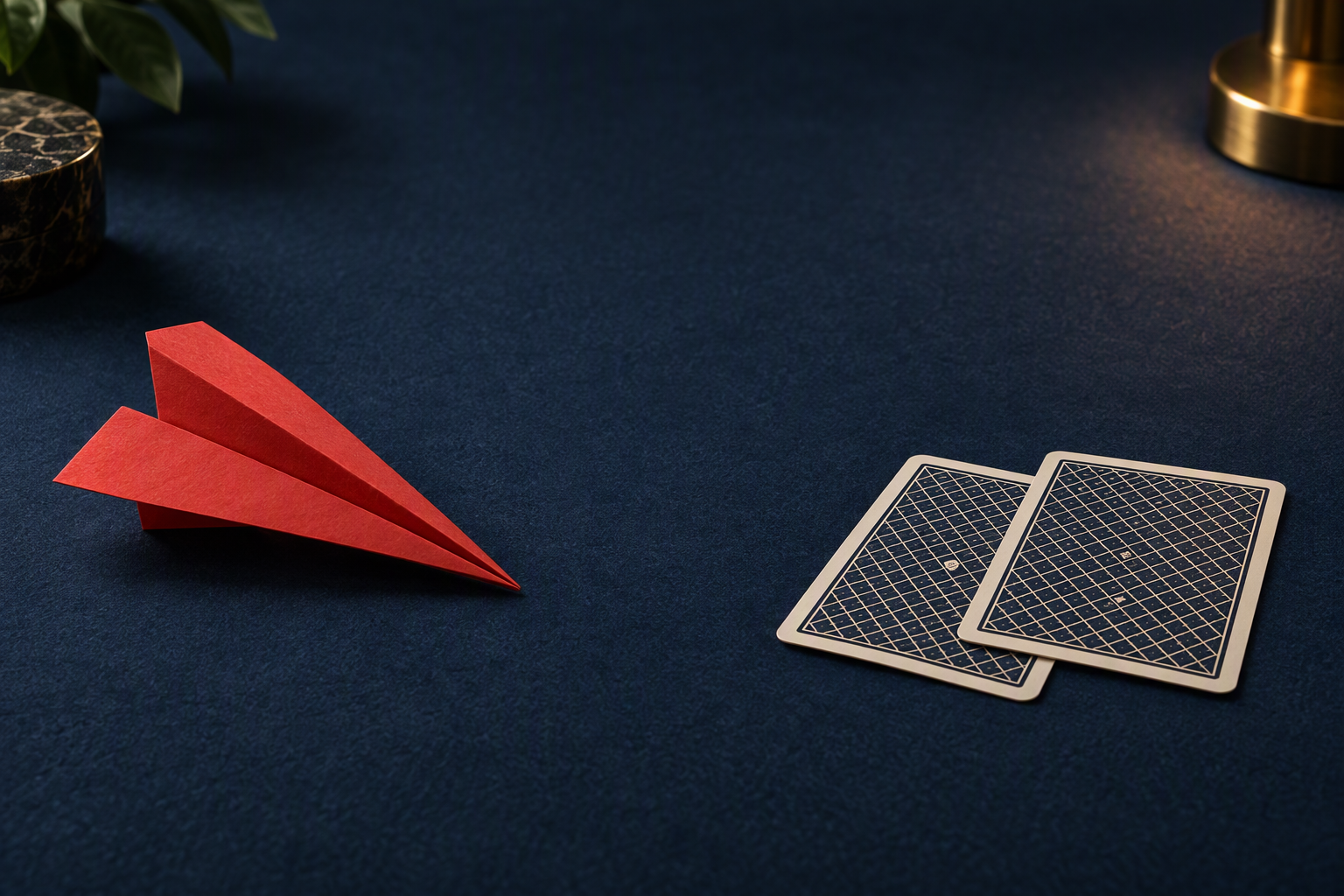 Red paper airplane beside two face-down playing cards on a navy tabletop